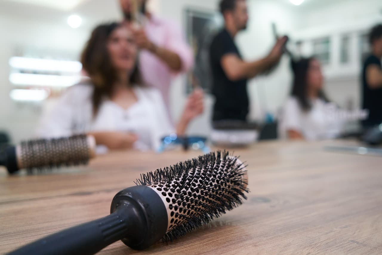 A round brush on the styling bench, a stylist at work in the salon behind